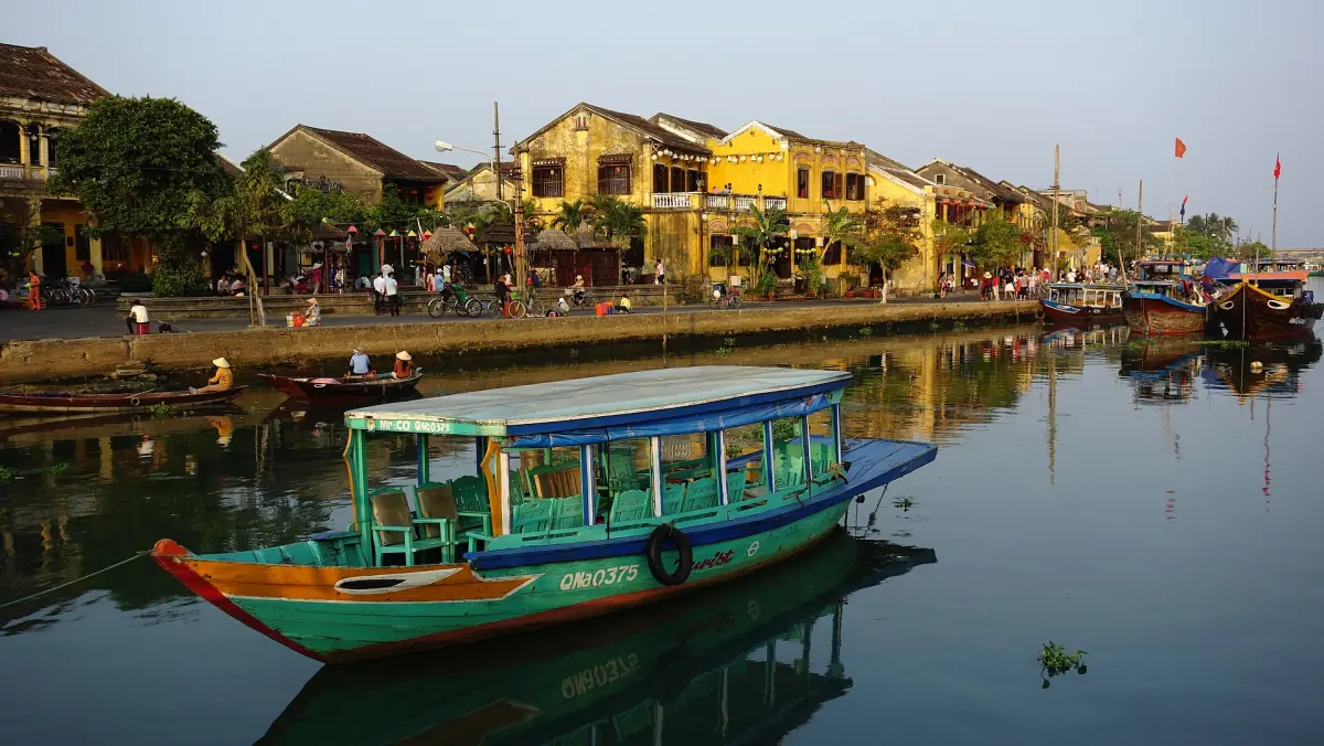 Ein Boot auf dem Thu-Bon-Fluss vor den gelben Häusern von Hoi An